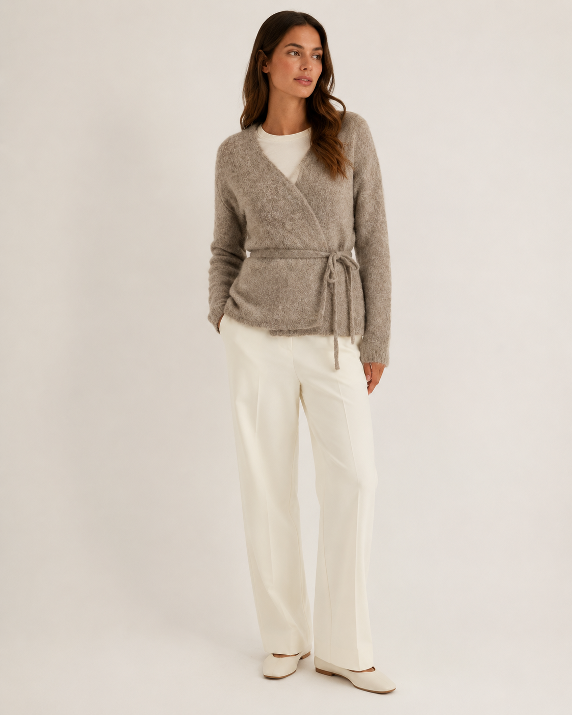 Beige kietaisuneulecardigan vyöllä, kokovartalokuva luonnonvalkoisella studiotaustalla