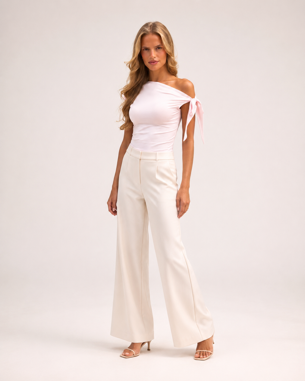 Modelo adulto de corpo inteiro com top Nova rosa-claro assimétrico e laço no ombro em estúdio off-white